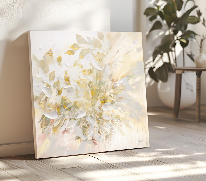 Square canvas art featuring a floral abstract design in white, cream, and gold. The artwork has a textured appearance with visible brushstrokes, creating a sense of depth and movement. The painting is leaning against a wall.