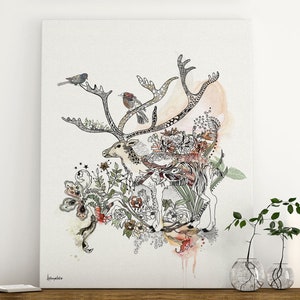 Canvas print featuring a detailed illustration of a reindeer adorned with intricate line art and watercolor accents. The reindeer is surrounded by a whimsical arrangement of flowers, leaves, and birds, creating a nature-inspired design. The artwork is predominantly in shades of beige, brown, and green, with pops of color from the flowers and birds. The artist's signature is subtly placed in the bottom left corner.
