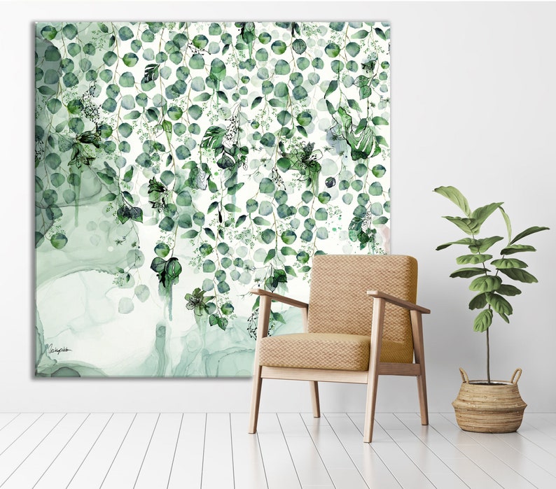 A large, abstract watercolor painting of green leaves and vines hanging down against a white background. The painting is displayed on a wall above a light brown armchair. A small potted plant is on the floor to the right of the chair.
