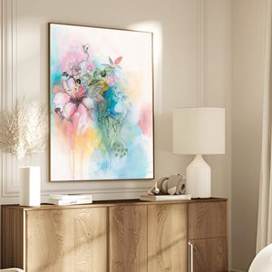 A watercolor painting of a pink flower with green leaves and blue accents on a white background. The painting is framed and hanging on a wall above a wooden dresser.
