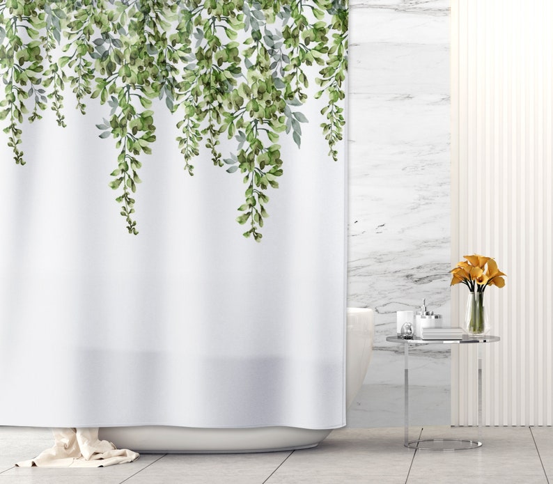 May include: White shower curtain with a green floral pattern of hanging vines. The curtain is in a bathroom with a white tiled wall and a white bathtub.