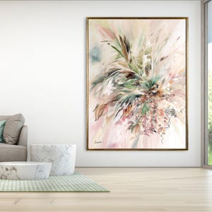 Large abstract painting with a gold frame. The artwork features a soft color palette of pink, green, and brown, with brushstrokes creating a floral or botanical design. The painting hangs on a white wall in a modern living room.