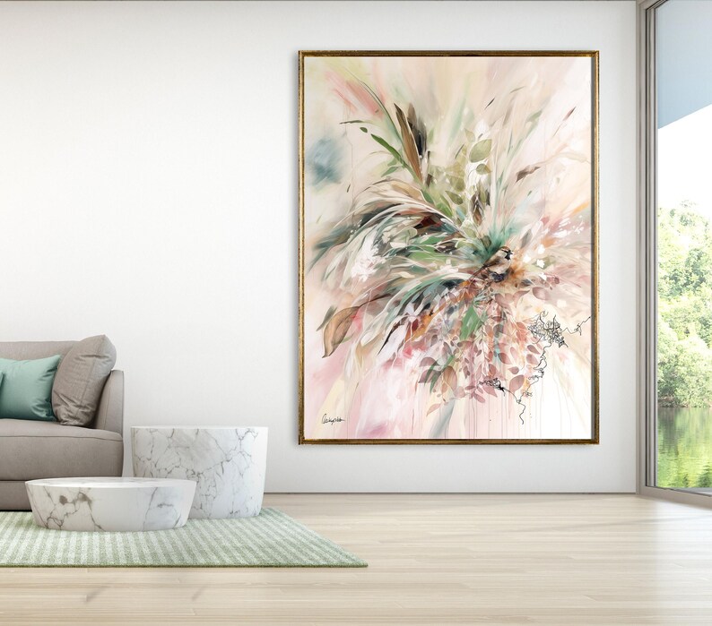 Large abstract painting with a gold frame. The artwork features a soft color palette of pink, green, and brown, with brushstrokes creating a floral or botanical design. The painting hangs on a white wall in a modern living room.