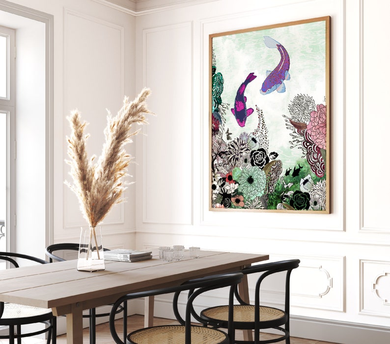 A framed illustration of two purple and pink fish swimming in a green and blue underwater scene with flowers and plants. The illustration is framed in a light wood frame and is hanging on a white wall.