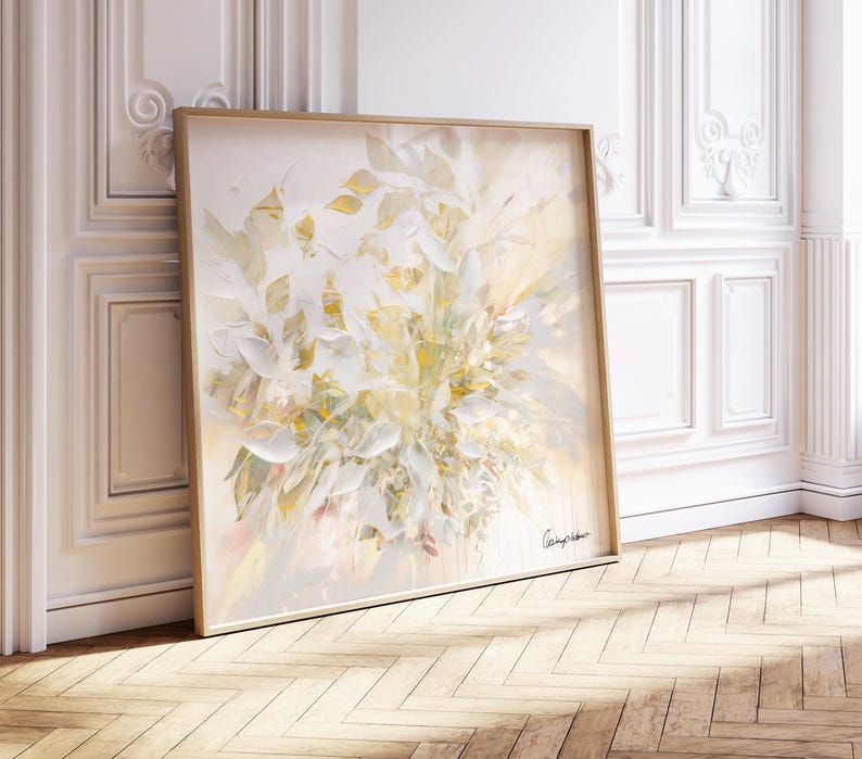 A large, square framed painting featuring an abstract floral design in soft, muted tones. The artwork showcases a bouquet of white and yellow leaves with subtle pink accents. The painting is leaning against a white wall with decorative molding.