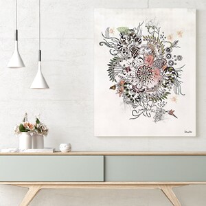 A black and white floral illustration with pink accents on a white background. The illustration is framed and hanging on a white wall above a light wood console table. The console table has a light gray drawer and is decorated with a white vase with pink flowers and a white diffuser.