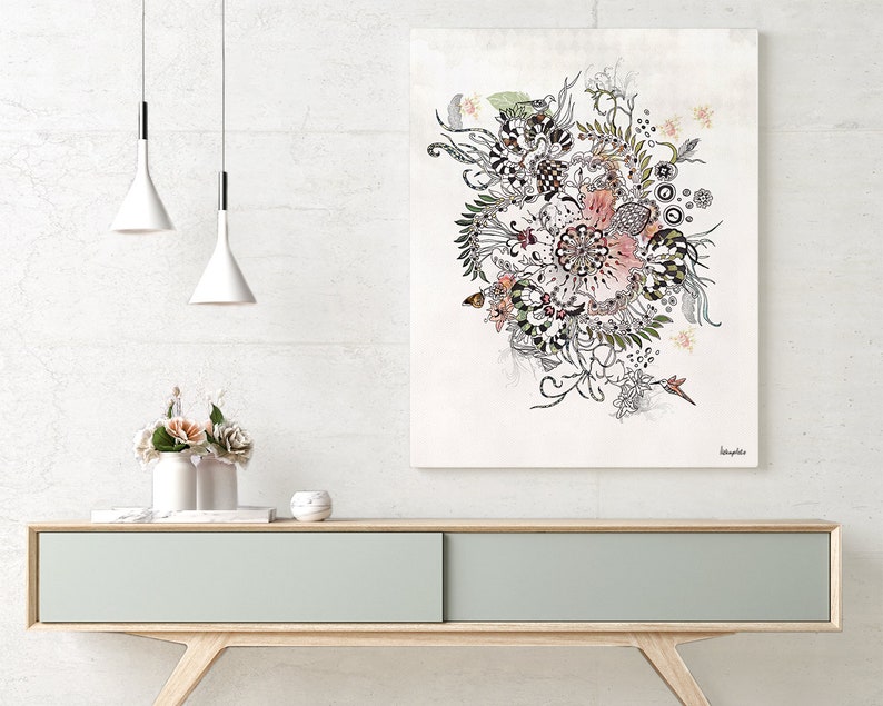 A black and white floral illustration with pink accents on a white background. The illustration is framed and hanging on a white wall above a light wood console table. The console table has a light gray drawer and is decorated with a white vase with pink flowers and a white diffuser.
