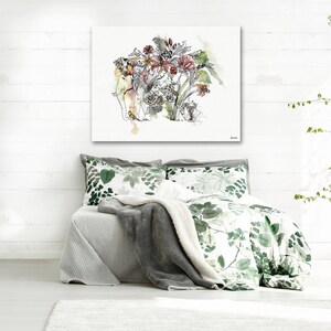 A watercolor painting of an elephant with a floral headdress hangs above a bed with green and white floral bedding. A gray blanket and pillows complete the bed set. The room has white walls and a white floor.