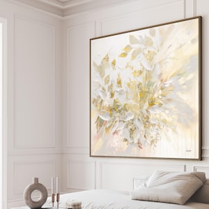 Large abstract painting with a wooden frame. The artwork features a cluster of white and gold leaf-like shapes against a soft, light background. The painting is displayed on a white wall.