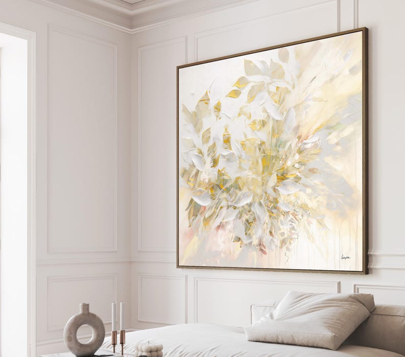Large abstract painting with a wooden frame. The artwork features a cluster of white and gold leaf-like shapes against a soft, light background. The painting is displayed on a white wall.