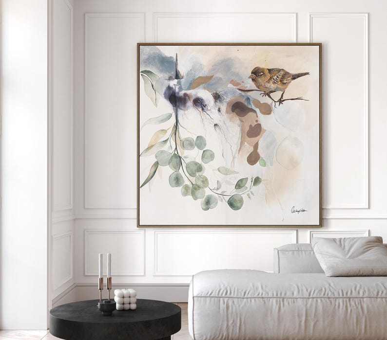 A square watercolor painting features a bird perched on a branch with eucalyptus leaves. The artwork is done in soft, muted tones of beige, brown, and green, creating a serene and calming atmosphere. The painting's style is abstract, with loose brushstrokes and flowing lines. The overall theme is nature-inspired, with a focus on organic shapes and textures.