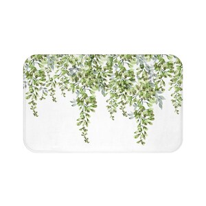 May include: A white bath mat with a green floral design. The design features cascading green leaves and flowers.