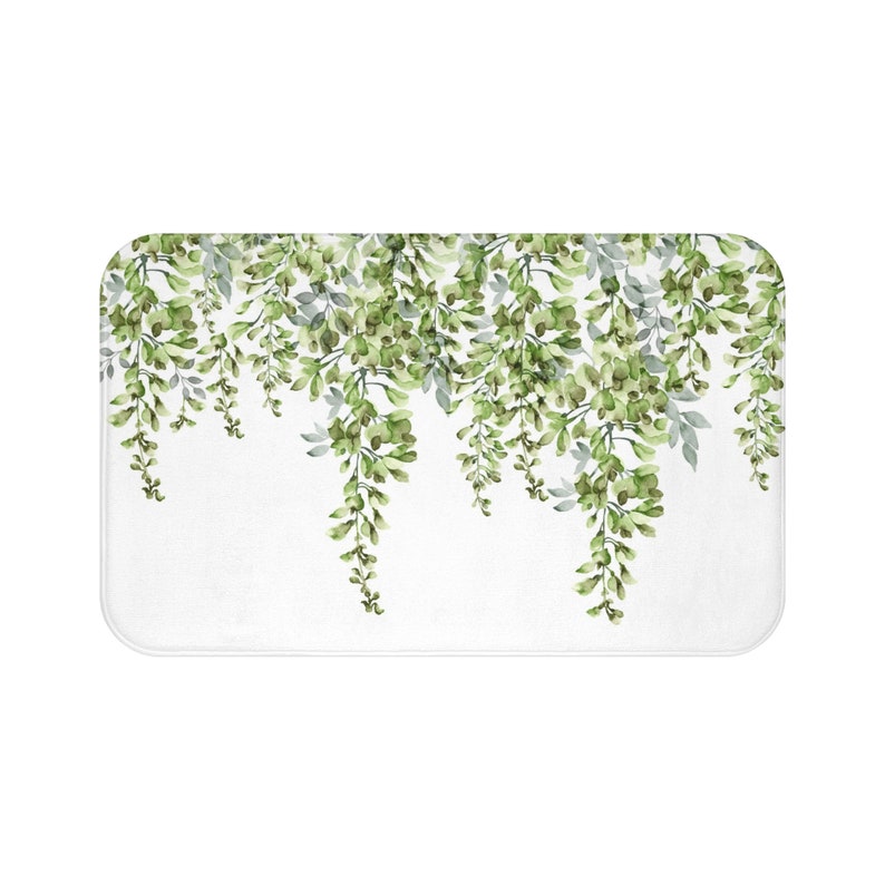 May include: A white bath mat with a green floral design. The design features cascading green leaves and flowers.