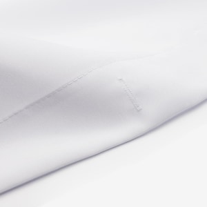 May include: Close-up of a white cotton fabric with a subtle texture. The fabric is folded and shows a seam along the edge.