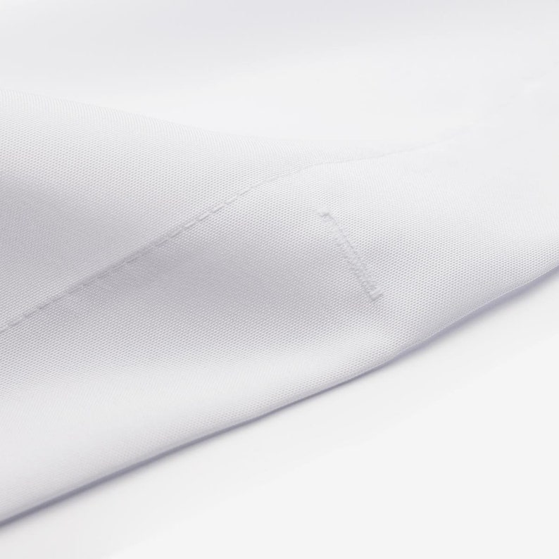 May include: Close-up of a white cotton fabric with a subtle texture. The fabric is folded and shows a seam along the edge.