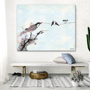 A watercolor painting of a bird perched on a branch with two other birds on a wire. The painting is framed and hanging on a white brick wall. The painting is in a living room setting with a white couch, a cactus plant, and a small potted plant with white flowers.