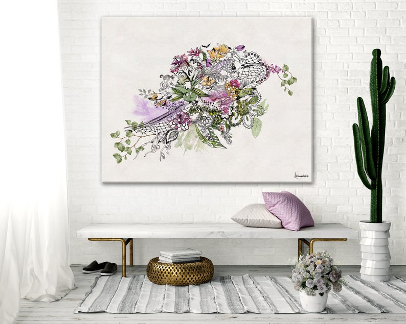 A white canvas print with a watercolor painting of a floral arrangement. The flowers are in shades of pink, purple, and yellow. The painting is surrounded by a white frame and is hanging on a white brick wall. The painting is in a living room setting with a white bench, a gold metal stool, and a potted cactus.