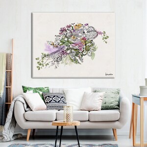 A white couch with green, white, and black patterned pillows. A small, round, wooden table with a glass candle holder sits in front of the couch. A white canvas with a black and white floral design hangs on the wall behind the couch. The canvas is signed 'Leanne Miller' in the bottom right corner.