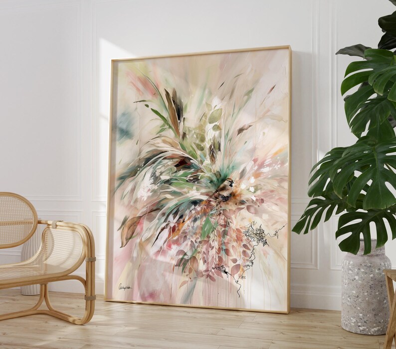 Large framed abstract art print featuring a floral design in soft pastel colors. The artwork includes green, pink, and brown tones, with a light beige background. The frame is a light wood color, and the overall style is modern.