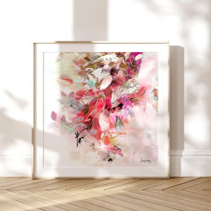 Abstract floral art print in a gold frame. The artwork features a vibrant mix of pink, red, and white brushstrokes, creating a soft, dreamy aesthetic. The composition includes leaf-like shapes and delicate lines, evoking a sense of nature and artistic expression.