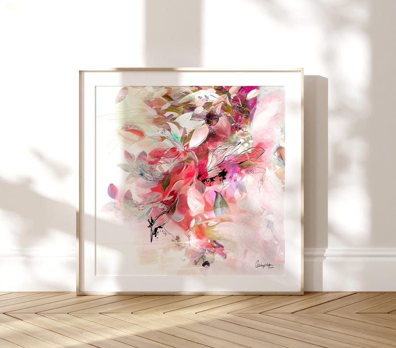 Abstract floral art print in a gold frame. The artwork features a vibrant mix of pink, red, and white brushstrokes, creating a soft, dreamy aesthetic. The composition includes leaf-like shapes and delicate lines, evoking a sense of nature and artistic expression.