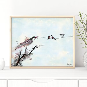 A framed watercolor painting of a bird perched on a branch with a twig in its beak. Two other birds are on a wire with a cat watching them. The background is a light blue sky with white clouds. The painting is signed 'Leannephillips' in the bottom right corner.