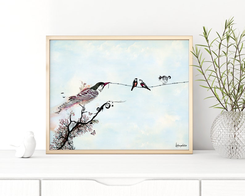 A framed watercolor painting of a bird perched on a branch with a twig in its beak. Two other birds are on a wire with a cat watching them. The background is a light blue sky with white clouds. The painting is signed 'Leannephillips' in the bottom right corner.