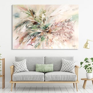 Abstract watercolor painting with a light pink, beige, and green color scheme. The painting features a cluster of leaves and branches in the center of the canvas. The leaves are painted in shades of green, brown, and pink. The branches are painted in shades of brown and beige. The painting is displayed on a wall above a gray sofa with green and white pillows.