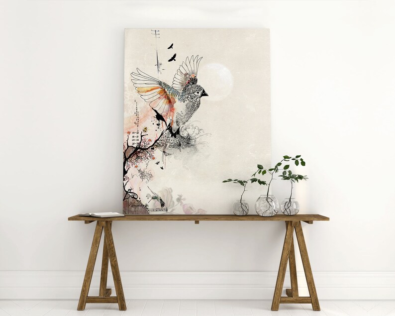 illustration of a bird with spread wings, set against a beige background with a watercolor effect. The bird is surrounded by delicate black branches and pink and orange watercolor accents. The image is framed and displayed on a white wall above a wooden table with three potted plants.
