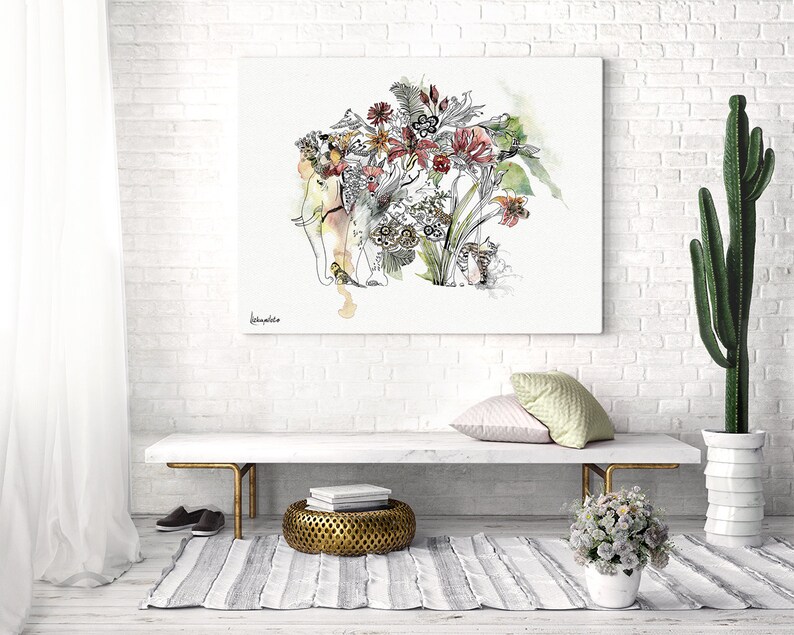 An artistic watercolor painting of an elephant with floral elements. The artwork is displayed on a white brick wall, with a bench, rug, and cactus in the foreground. The painting has a light color palette with red, green, and yellow accents.