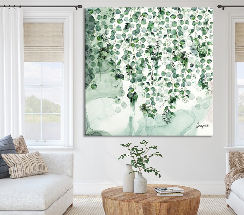 A square canvas print with a watercolor style design of green leaves and branches on a white background. The leaves are arranged in a cascading pattern, creating a sense of movement and depth. The artwork is signed in the bottom right corner with the artist's name.