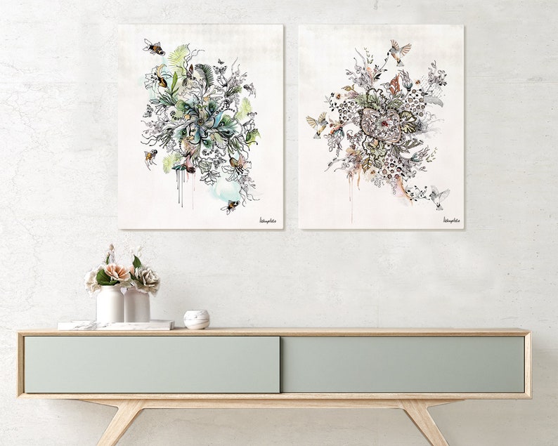 Two framed watercolor paintings with a floral theme. The paintings feature intricate details of flowers, leaves, and birds. The paintings are displayed on a light wood shelf with a light gray drawer.