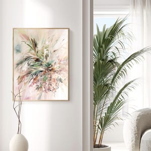 Abstract floral art print in a wooden frame. The artwork features a soft color palette of pink, green, and beige, with brushstrokes creating a dynamic, textured composition. The painting is displayed on a white wall.