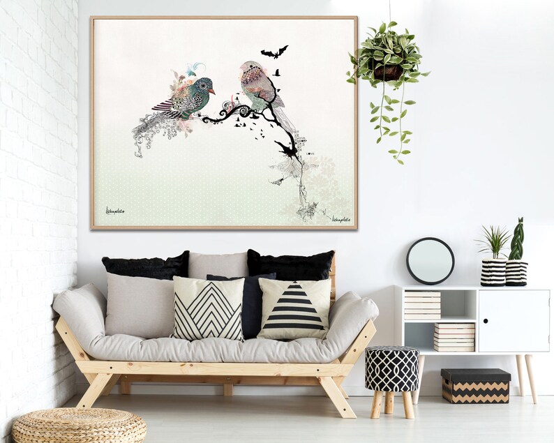 A framed art print featuring two stylized birds perched on a branch with a green and white background. The birds are decorated with intricate patterns and details. The print is framed in a light wood frame.