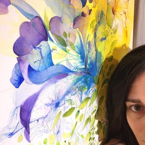 Abstract watercolor painting with a vibrant mix of blue, purple, yellow, and green hues. The painting features a large, central flower-like shape with delicate lines and overlapping layers of color.