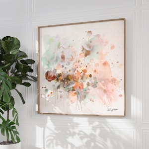 Abstract floral watercolor painting in a wooden frame. The artwork features a blend of soft colors, including peach, green, and brown, with splatters and drips creating a dynamic composition. A signature is visible in the bottom right corner.