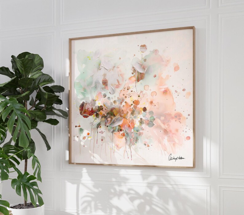 Abstract floral watercolor painting in a wooden frame. The artwork features a blend of soft colors, including peach, green, and brown, with splatters and drips creating a dynamic composition. A signature is visible in the bottom right corner.