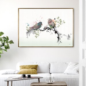 rectangular wall art print featuring two birds perched on a stylized black branch. The bird on the left has teal and pink plumage, while the bird on the right is soft pink and grey. The design includes green leaves and pink splatters.