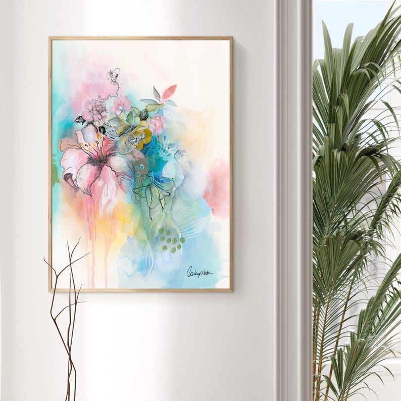 A framed abstract watercolor painting with a light pink, blue, and yellow background. The painting features a cluster of pink flowers with green leaves and stems. The painting is signed in the bottom right corner.