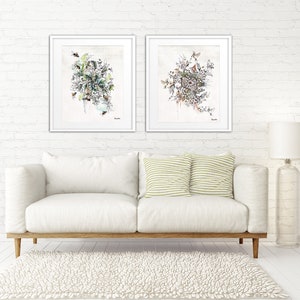 Two framed watercolor paintings of floral arrangements with a white background. The paintings are hanging on a white brick wall above a white couch with two green and white striped pillows.