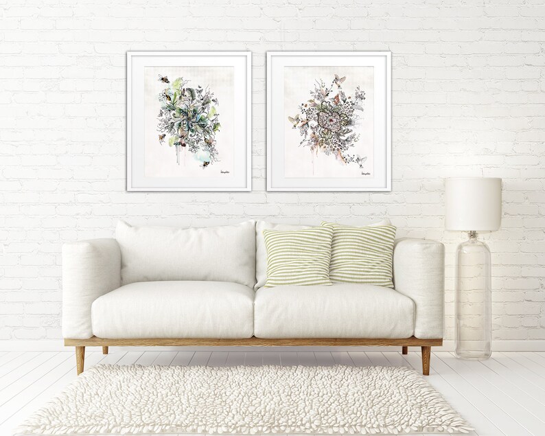 Two framed watercolor paintings of floral arrangements with a white background. The paintings are hanging on a white brick wall above a white couch with two green and white striped pillows.
