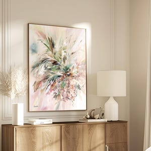 Abstract floral art print in a wooden frame. The artwork features a soft color palette of pink, green, and brown, with a focus on botanical elements. The painting is displayed above a wooden cabinet.