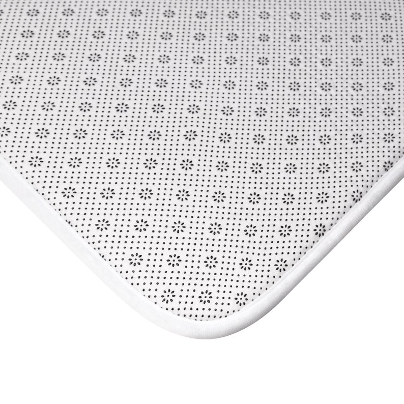 May include: Close-up of the underside of a white bath mat with a black non-slip pattern. The mat has a white border.