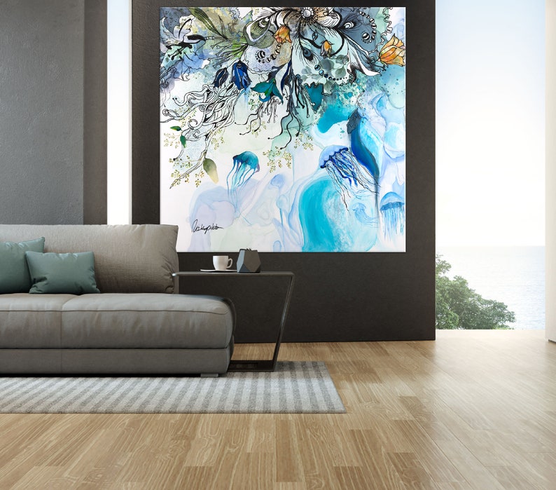 Abstract watercolor painting featuring blue jellyfish and floral elements in shades of blue, green, and white. The painting is framed and hanging on a wall in a modern living room.