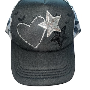 May include: Black trucker cap with a mesh back and a curved peak. The front has a heart and two stars, one silver sequined and one black sequined. Small bat silhouettes are scattered across the top.