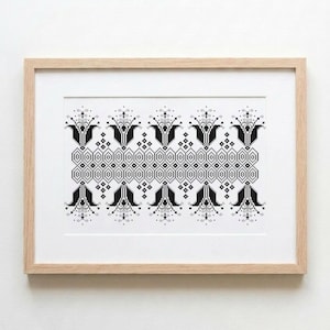 May include: A framed cross-stitch embroidery piece featuring a repeating black geometric and floral pattern on a white background. The design consists of symmetrical stylized flower motifs and diamond shapes enclosed in a light-colored wooden frame.