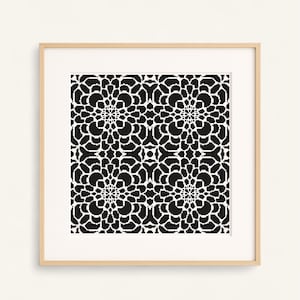 Peut inclure: Une impression encadrée présentant un motif floral noir et blanc. Le motif est symétrique, avec des formes florales répétitives. L'œuvre est encadrée dans un cadre en bois clair, créant un contraste avec le fond blanc.