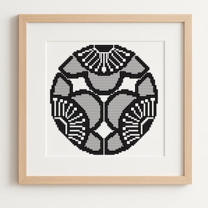 Peut inclure: Une œuvre d'art murale encadrée présentant un motif circulaire pixélisé en noir et blanc. Le graphique se compose de formes florales symétriques répétitives disposées en motif radial, le tout dans un cadre en bois clair.