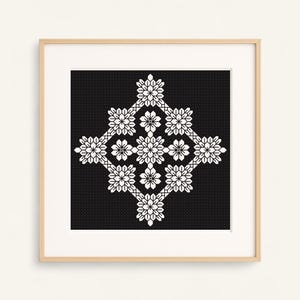 Peut inclure: Un motif de point de croix encadré, présentant un motif floral symétrique blanc sur fond noir. L'œuvre est encadrée dans un cadre en bois clair, créant un contraste. Le motif floral est le point central de l'image.