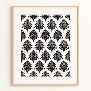 May include: A framed print with a repeating pattern of black and grey floral motifs on a white background. The design has a damask-like quality, with each element resembling a symmetrical tree or flower. The frame is a light wood colour.